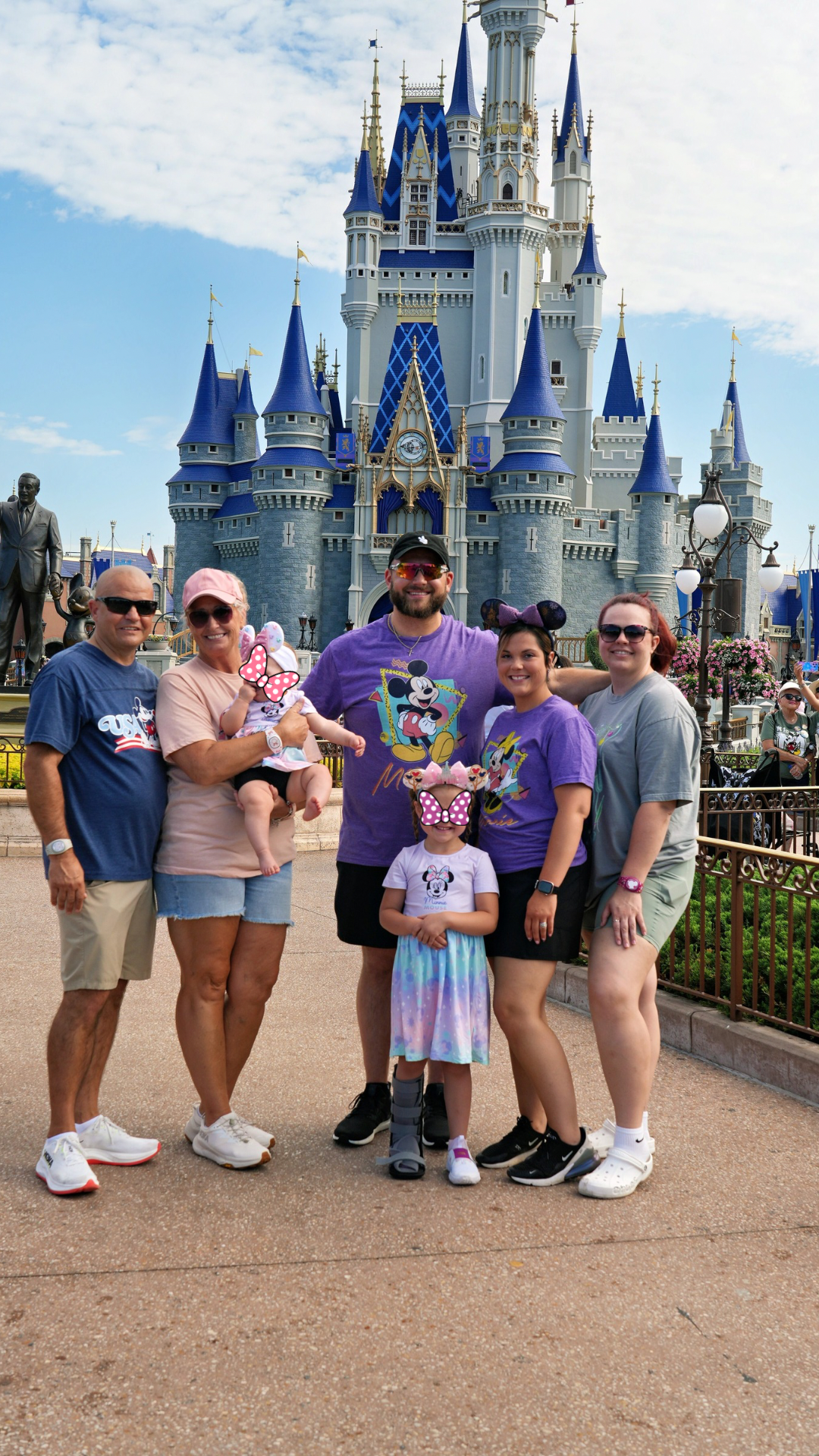 The Pixie Packed Family together in front of Cinderella Castle at Magic Kingdom, with the two youngest children's faces covered by pink Minnie bows for privacy